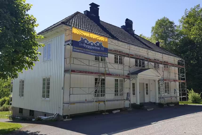 Stort trehus under maling i Asker, med DinByggpartner-banner på stillaset